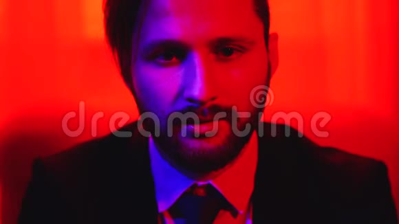 一个留着胡子的微笑的男人在明亮的红光背景下看着相机视频的预览图