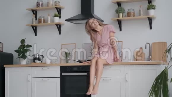 快乐的女孩坐在厨房的桌子上无忧无虑地晃着腿视频的预览图
