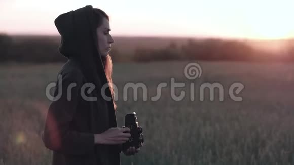 女性站在田野上带着老式相机在背景夕阳下带着阳光视频的预览图