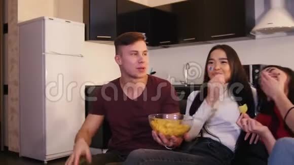 一群年轻的朋友在一起看电视和聊天一个年轻人拿着装满薯片的碗视频的预览图