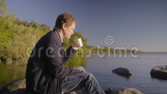 穿着紧身衣的男人躺在大石头上喝着咖啡视频的预览图