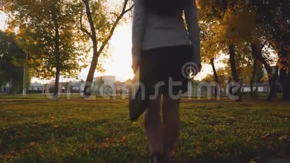 商务女性带着公文包在夕阳下在公园的草坪上走下腿部特写视频的预览图