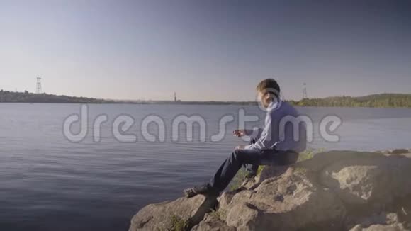 一个人坐在河岸上的石头上把石头扔进水里视频的预览图