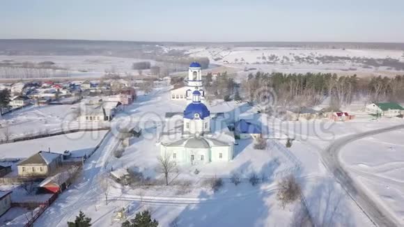 俄罗斯白色东正教教堂的鸟瞰图蓝色圆顶和金色十字架位于小村庄附近视频的预览图