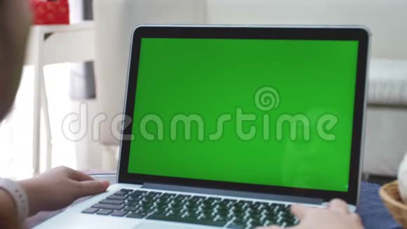 过肩射的亚洲女子看着绿屏办公室人员使用带有笔记本电脑绿色屏幕的笔记本电脑视频的预览图