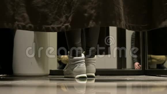 从地面透视在商店试衣间的窗帘后面穿着运动鞋的女人的腿视频的预览图