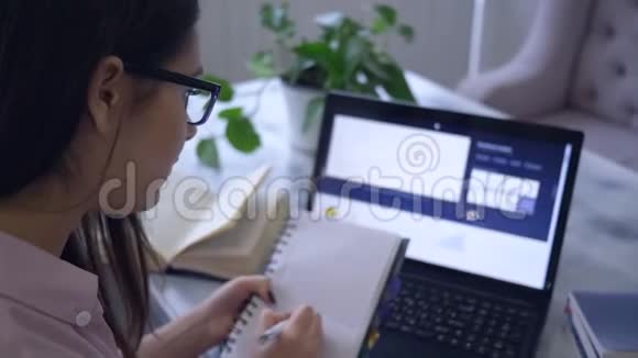 远程在线学习学生女孩使用笔记本电脑设备并在记事本中绘制一个图形坐在咖啡馆的桌子上视频的预览图