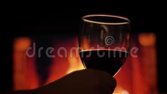 近景后景拍摄双手捧着一杯红酒背景上有温暖的壁炉和火焰视频的预览图