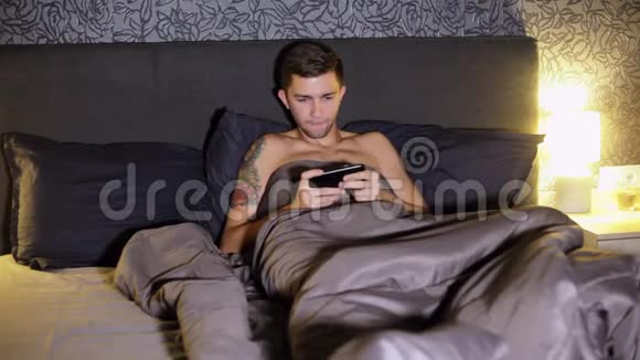 年轻人晚上躺在家里的床上玩智能手机游戏紧张的比赛赢得比赛并且是视频的预览图