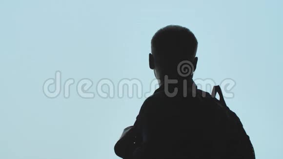 一个背着背包的年轻人的剪影看着飞机在蓝天上起飞视频的预览图