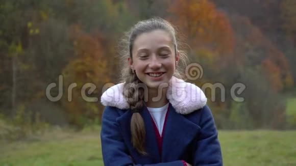 一个美丽的年轻女孩站在秋林里看着相机微笑着她高兴慢动作视频的预览图