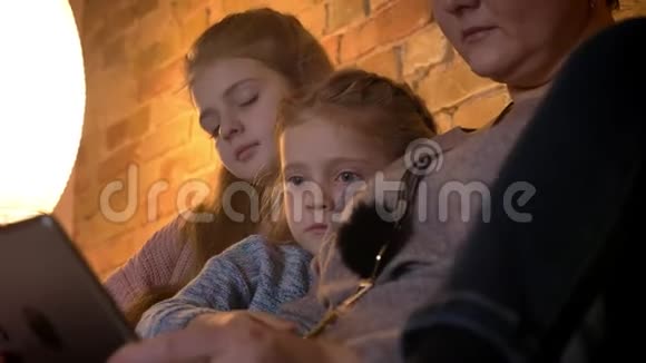 两个高加索小女孩在舒适的家庭氛围中专心观看平板电脑的特写镜头视频的预览图