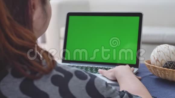 过肩射的亚洲女子看着绿屏办公室人员使用带有笔记本电脑绿色屏幕的笔记本电脑视频的预览图