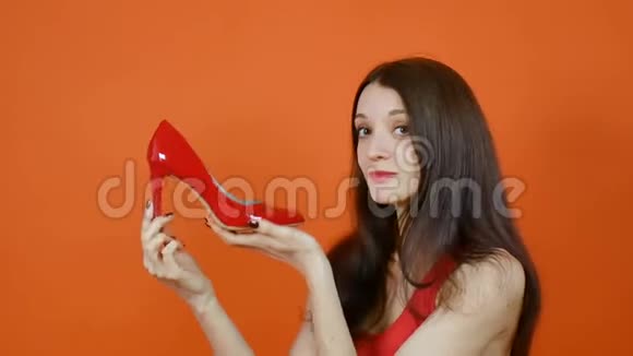 一个漂亮的棕色头发的年轻女孩检查一双红色的鞋子情感一幅橙色画室里的画视频的预览图