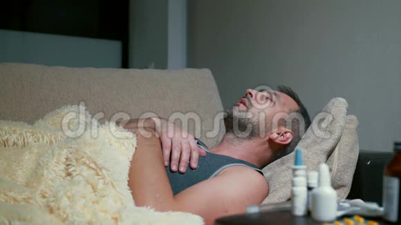 病人躺在沙发上咳嗽一个病人躺在裹着毯子的沙发上视频的预览图