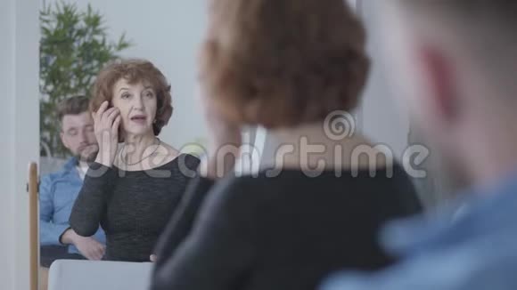 漂亮的年长的成熟女人看着镜子里的倒影摸着坐在年轻人面前的头发视频的预览图