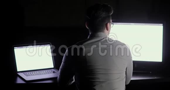 程序员正在办公室加班深夜坐在工作场所的两个监视器前视频的预览图