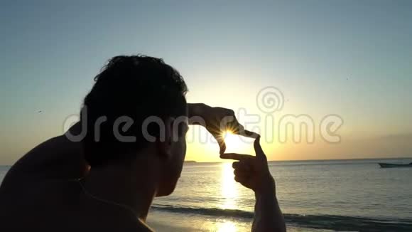 在海滩上令人惊叹的日落时分一个卷发青年用双手制作相框摄影师剪影视频的预览图
