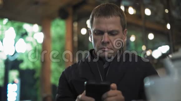 一个悲伤的人在智能手机上观看照片坐在夜店等待约会视频的预览图