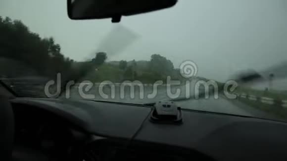 在恶劣的雨天驾驶仪表板和方向盘与司机手雨滴在车窗挡风玻璃上视频的预览图
