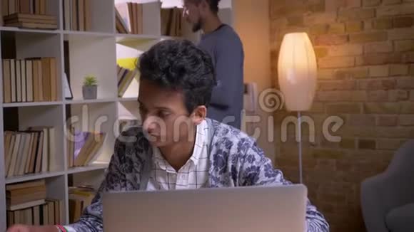 两名文化多样性学生在室内大学图书馆学习的特写镜头印度男性在线学习视频的预览图