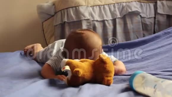 熟睡的刚出生的小男孩趴在肚子上爬行伸手去软玩具小狗和奶瓶视频的预览图