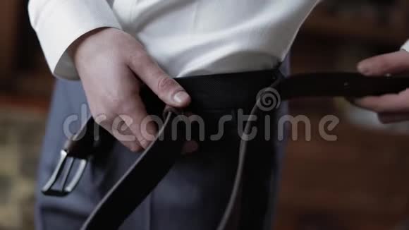 英俊的新郎用裤子把皮带固定好结婚的早晨商人视频的预览图