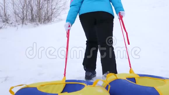 女人爬上高高的雪山手里拿着雪碟在寒冷的冬日女孩手里拿着视频的预览图