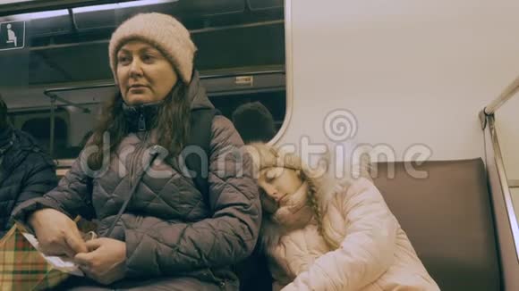 疲惫的妈妈和熟睡的女儿在现代城市的地铁里开车视频的预览图