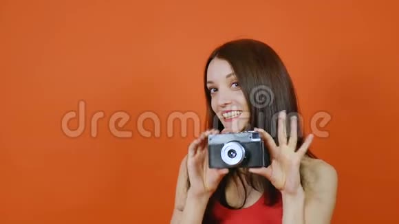 美丽的棕色头发的年轻女孩手里拿着相机情感一幅橙色背景的画室里的艺术肖像视频的预览图