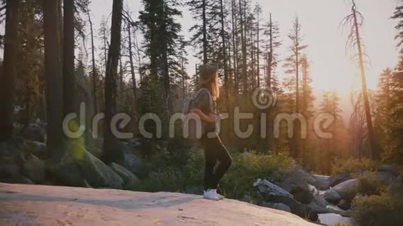 镜头围绕着兴奋的旅游女孩站在Yosemite森林深处的大岩石上令人难以置信的日落慢镜头视频的预览图