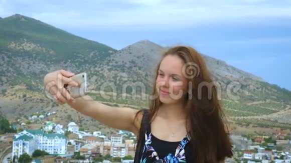 一个女孩在山和天空的背景下自拍的肖像视频的预览图