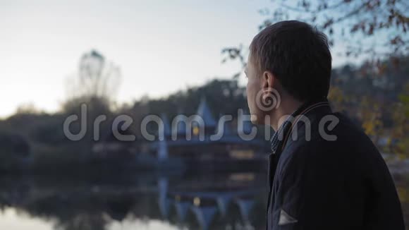 特写镜头悲伤的男人在湖边的秋天公园喝茶视频的预览图