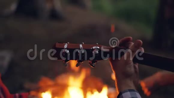 男游客的特写镜头晚上在露营地弹吉他背景是燃烧的火焰视频的预览图