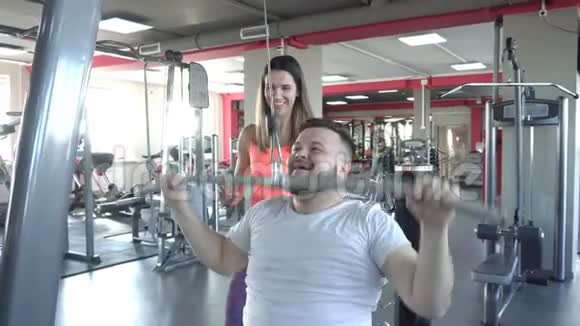 胖白种人留着胡子的男人在健身房里和女教练一起练习推力视频的预览图