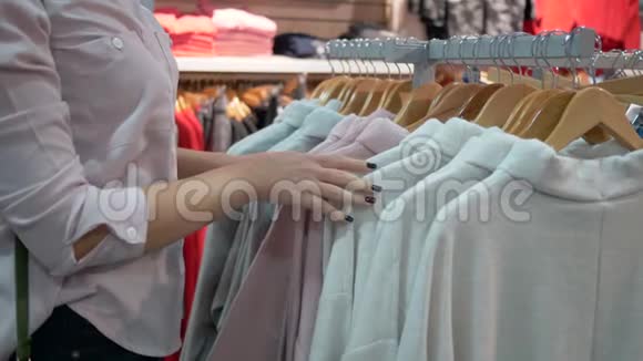 时尚购物女性的双手在季节性折扣期间在商店的衣架上选择时尚的新衣服并尝试视频的预览图