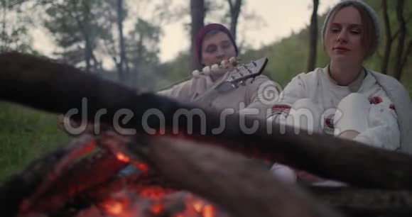 一对年轻夫妇坐在炉火旁吃棉花糖谈笑风生视频的预览图