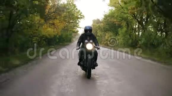 秋天一个戴着墨镜和皮夹克的年轻人骑着摩托车骑在柏油路上的正面景色视频的预览图