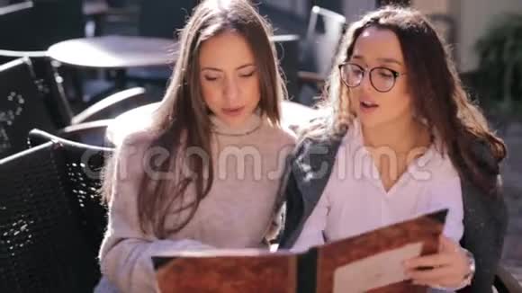 两个年轻漂亮的女人在餐馆里看菜单翻页选择吃早餐视频的预览图