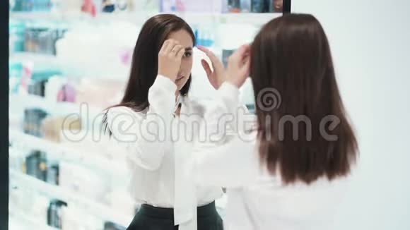 在化妆品店里漂亮的年轻女子在镜子前打扮自己视频的预览图