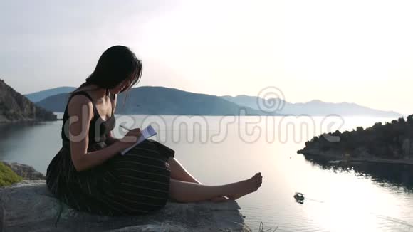 一个女人在一本笔记本上写字她坐在高高的海面上动作缓慢视频的预览图