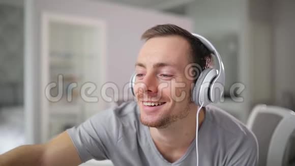 快乐的微笑男人在家里用耳机听音乐视频的预览图