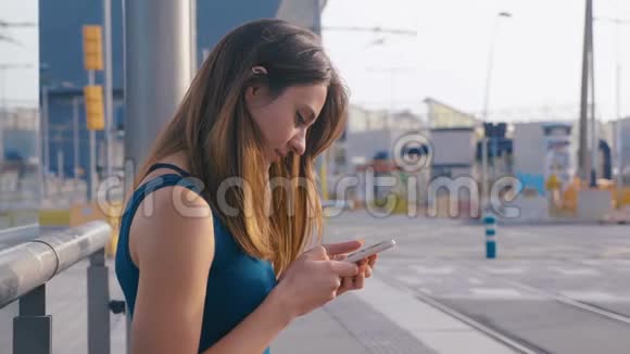 年轻迷人的女人坐在公共汽车或地铁车站女孩用她的手机输入信息在等她视频的预览图