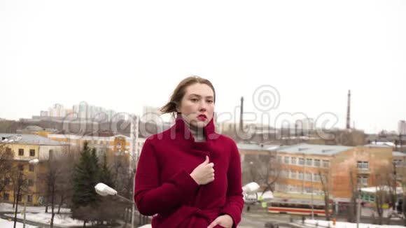 冬天在背景城市的屋顶上摆模特媒体漂亮的年轻女子穿着红色外套在屋顶上摆姿势视频的预览图