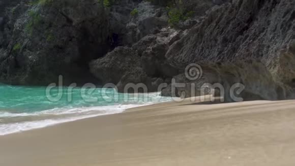 清澈透明的海浪溅在沙质海岸的悬崖背景上悬崖岛上的绿松石海水蓝色海洋视频的预览图