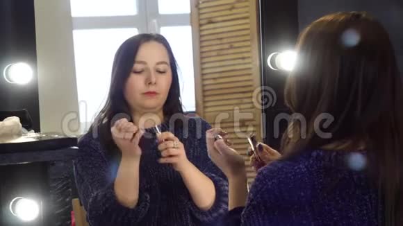 年轻女子在照相馆画嘴唇媒体女人用灯泡在镜子里固定化妆色调的嘴唇敷料视频的预览图