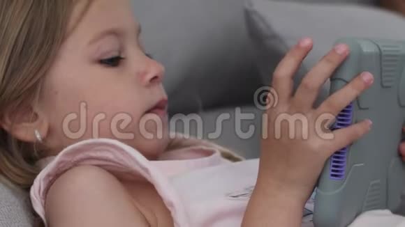 沙发上躺着一个年轻女孩的特写镜头她拿着一个放在灰色保护套里的平板电脑视频的预览图