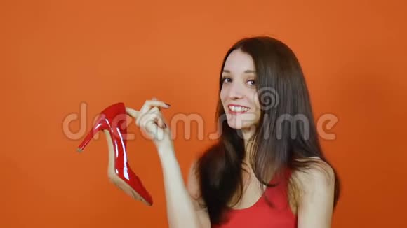 一个漂亮的棕色头发的年轻女孩检查一双红色的鞋子情感一幅橙色画室里的画视频的预览图
