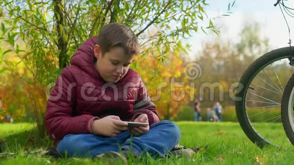 十几岁的男孩坐在草地上玩智能手机视频的预览图