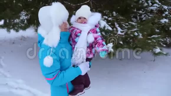 妈妈抱着她的小女儿在白雪皑皑的冬松公园沿路散步笑了起来圣诞周末快乐的母亲视频的预览图